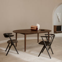 Oval wooden table in rich brown, complemented by black chairs and neutral decor accents against a light beige wall.