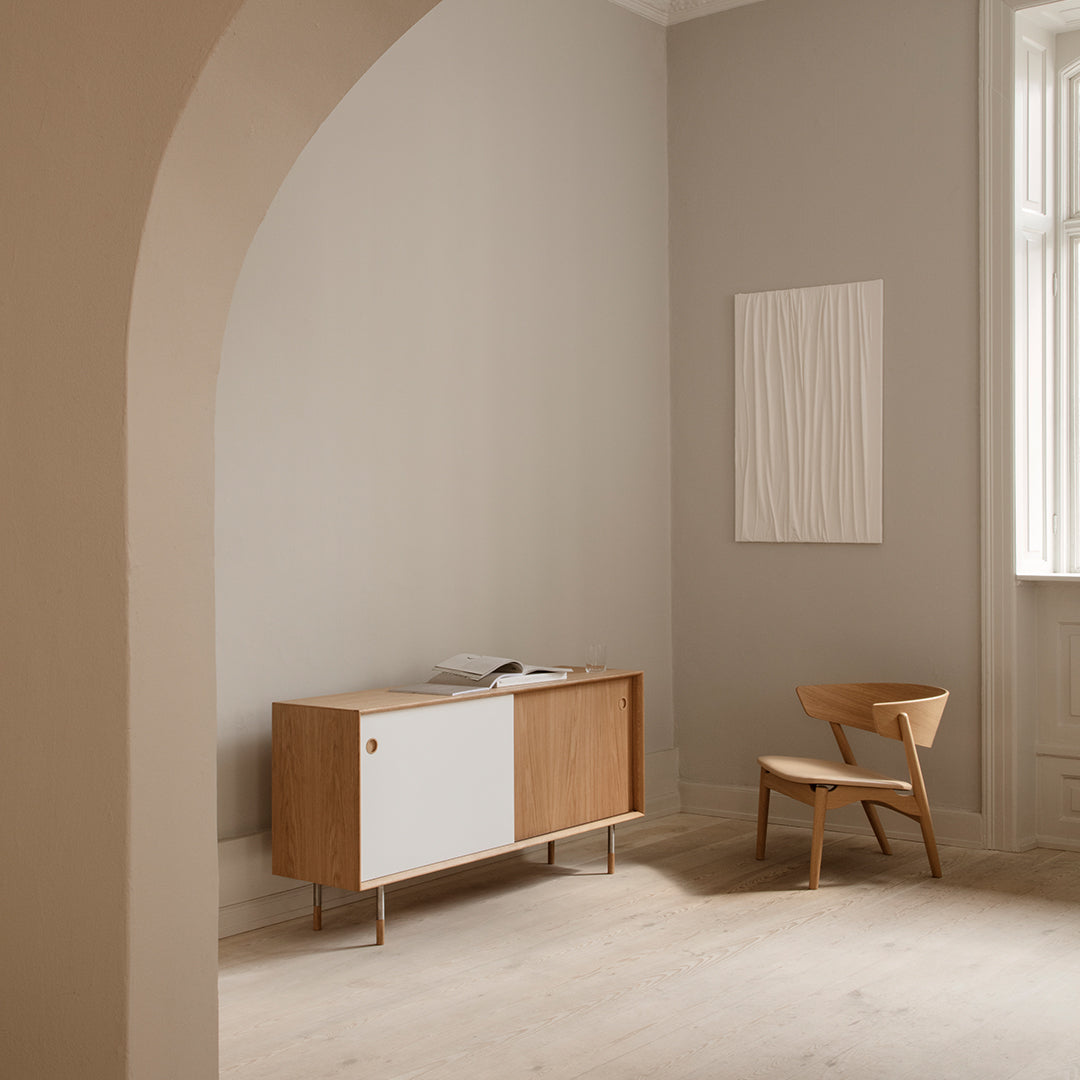 Modern wooden sideboard with white and natural oak accents, set against neutral gray walls and minimal decor.
