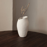 White ceramic vase with a textured surface, showcasing a minimalist design against a warm, wooden table.