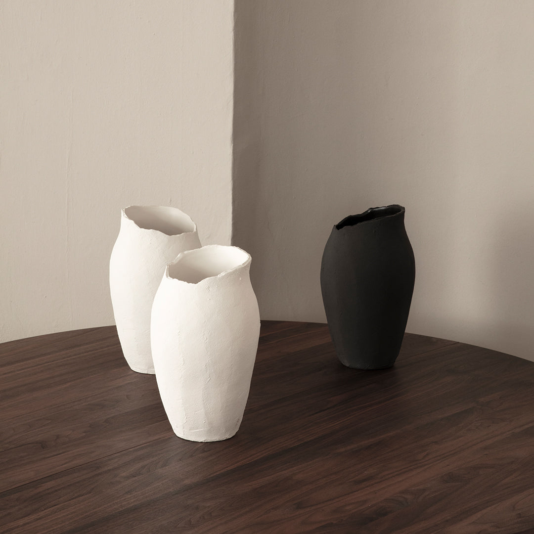 Set of three vases in matte white and black colors, featuring organic shapes and textured finishes on a wooden table.