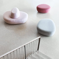 Soft pastel poufs in pink, lavender, and light gray, featuring organic, rounded shapes on a minimalist floor.