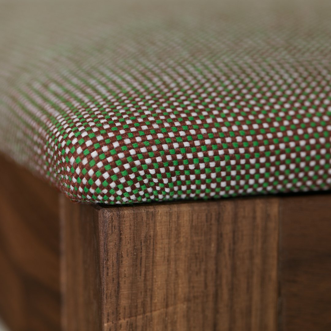 Brown and green checkered fabric with contrasting red and white dots on cushioned seat edge.