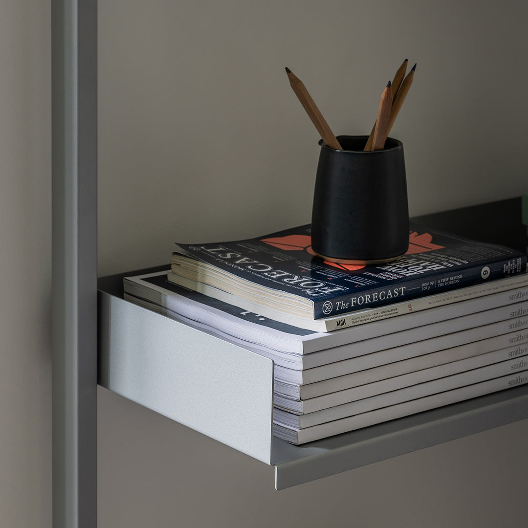 Black pencil holder with pencils atop stacked white and blue patterned books on a sleek gray shelf.