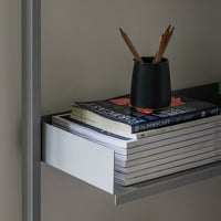 Black pencil holder with pencils atop stacked white and blue patterned books on a sleek gray shelf.
