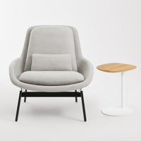 Gray upholstered chair with a minimalist design, featuring a light gray cushion and contrasting black legs next to a wooden side table.
