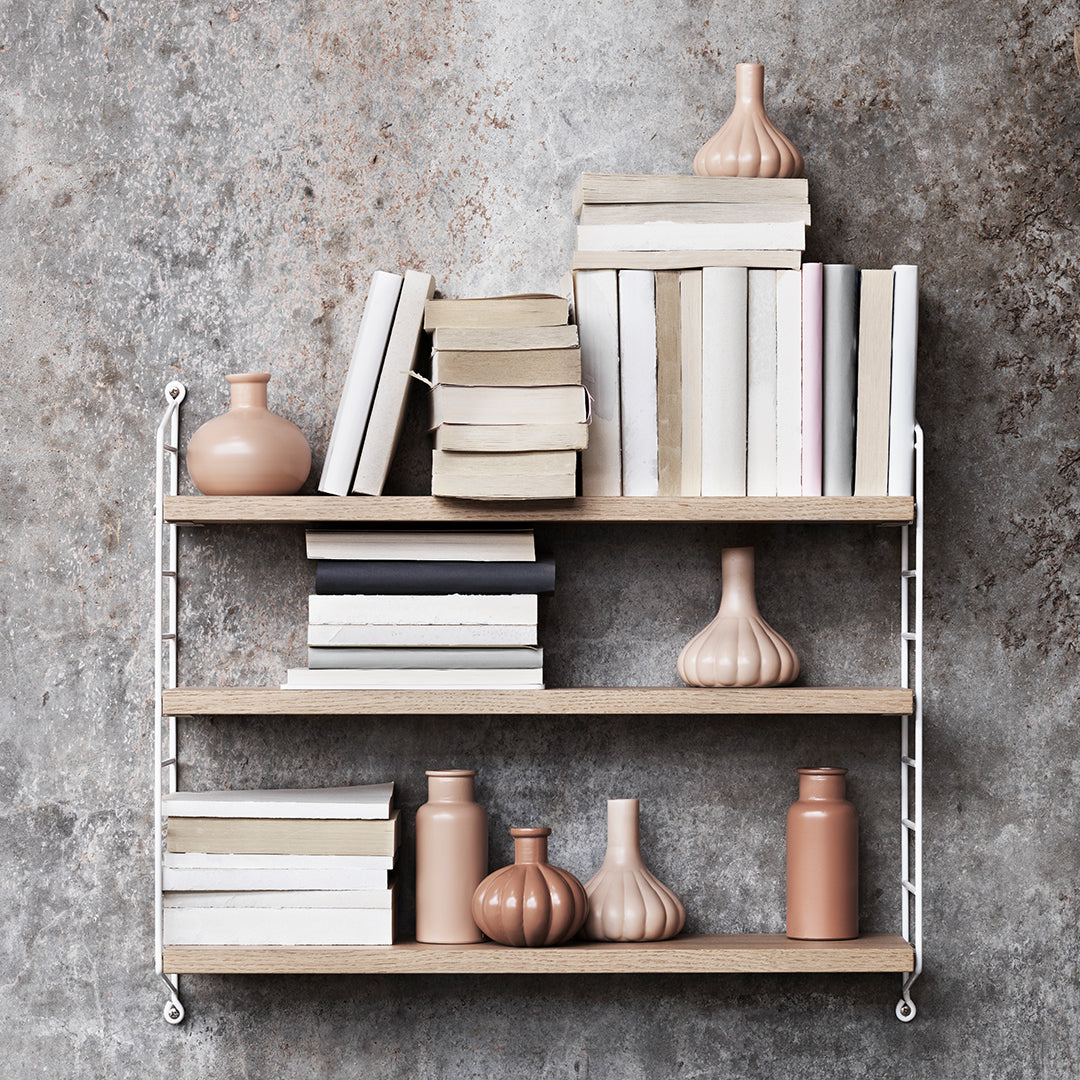 Shelves featuring neutral-colored books and soft peach vases against a textured gray wall background.
