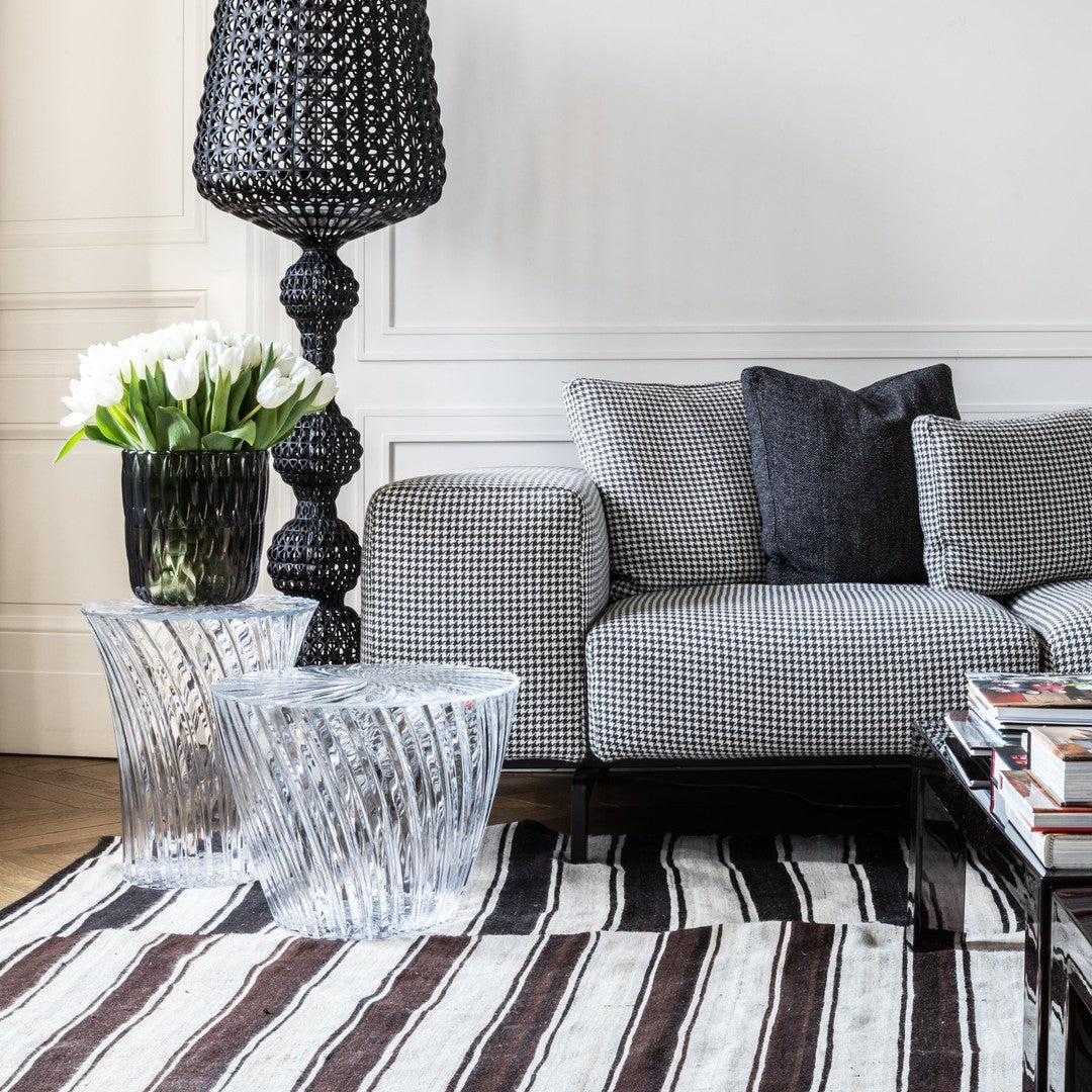 "Black and white houndstooth sofa, clear glass tables, layered striped brown and cream rug, vibrant green tulips."