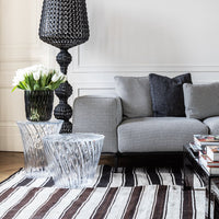 "Black and white houndstooth sofa, clear glass tables, layered striped brown and cream rug, vibrant green tulips."