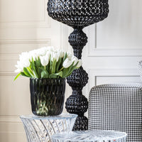 Elegant black woven lamp, glossy black vase with white tulips, and clear textured tables with houndstooth-patterned chair.