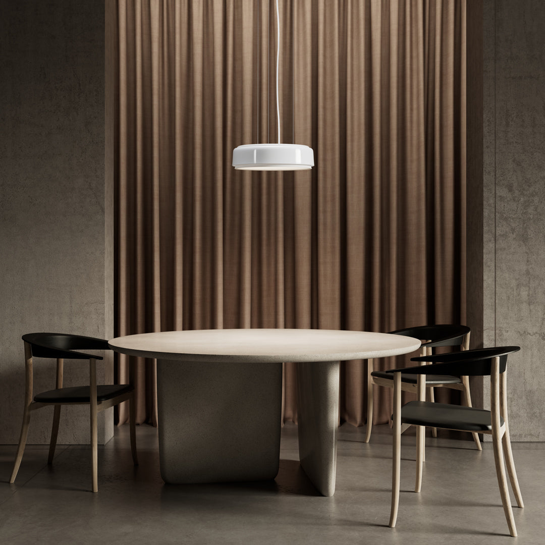 Round table with a smooth light gray surface, accompanied by black chairs against a backdrop of warm beige curtains.
