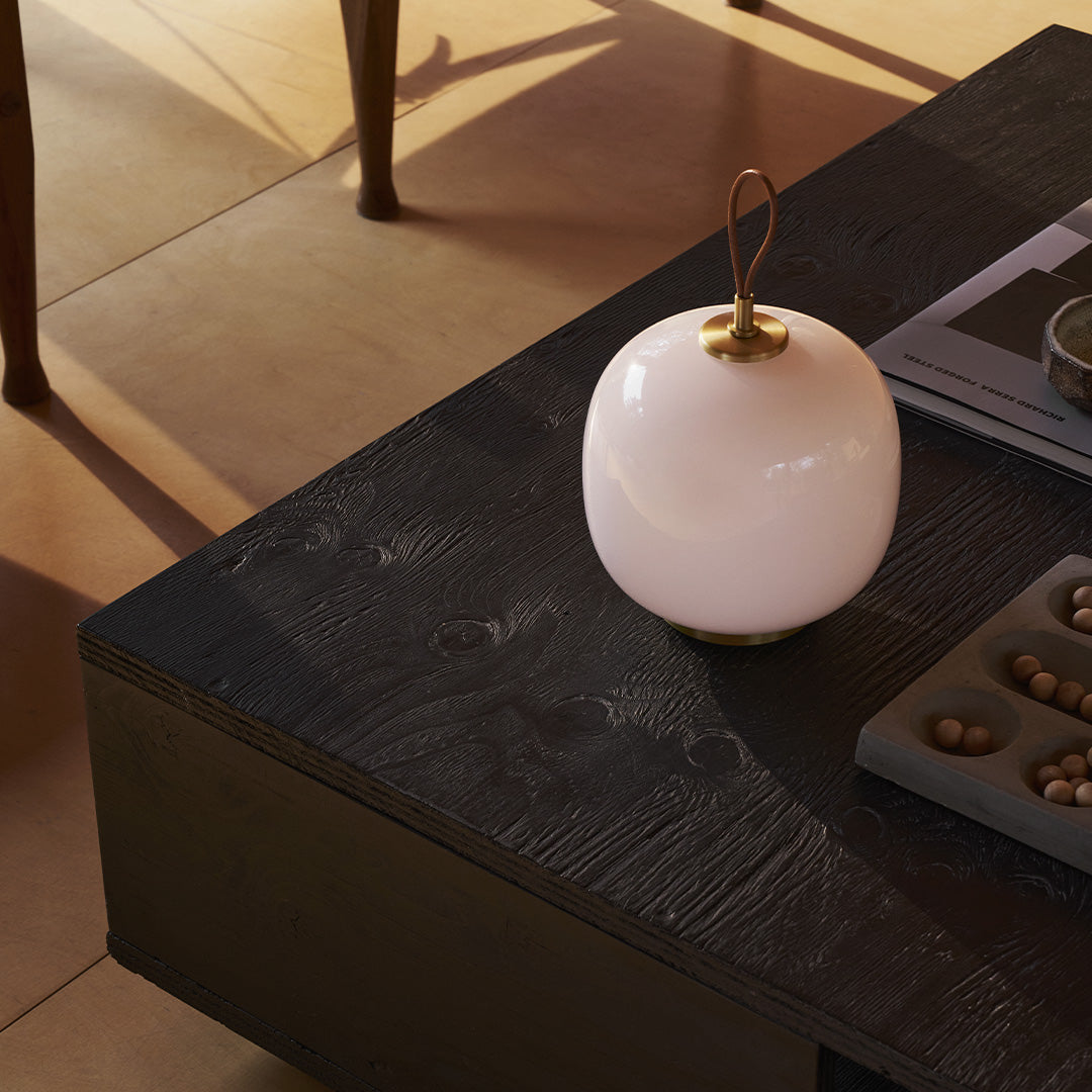 Glossy white lamp with gold accents on a textured black wood table, surrounded by neutral-toned decor.