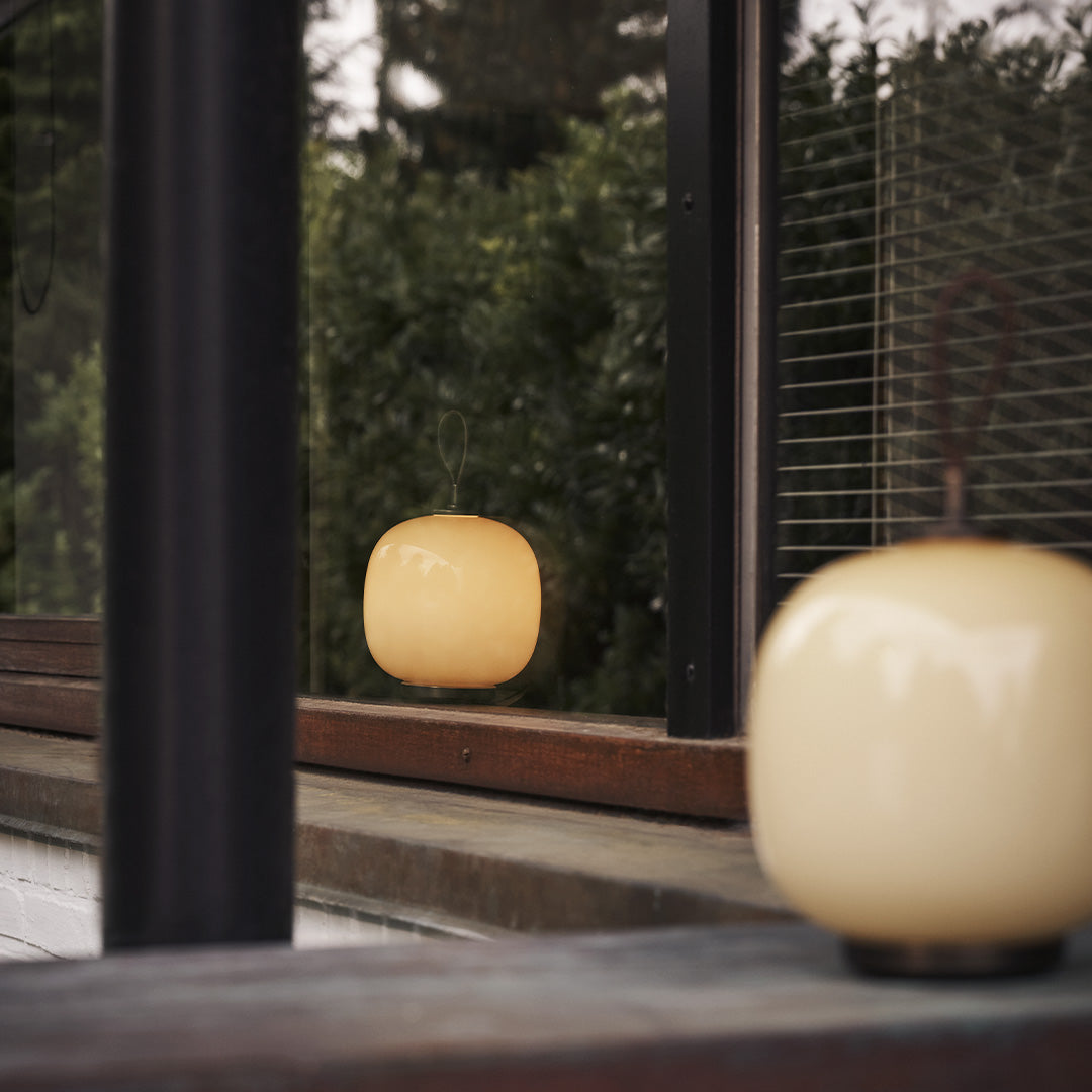 Soft yellow glass lamp with a rounded pattern, set against a dark wood backdrop and green foliage reflection.