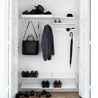 Stylish white closet with black shoes, hats, and a gray coat; sleek and modern design with clean lines.