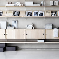 Light wood shelving unit with minimalist black accents and a neutral background, displaying magazines and decor items.