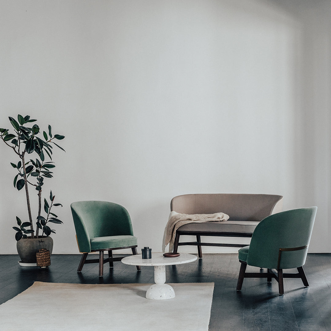 Stylish green velvet chairs and a beige sofa on a minimalist backdrop, featuring soft textures and earthy tones.