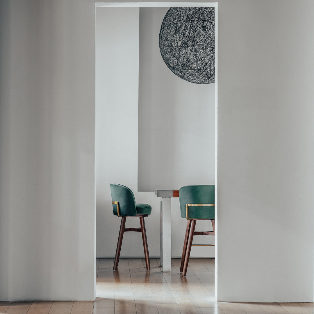 "Elegant green chairs with wooden legs against a minimalist gray wall, featuring a circular decorative piece."