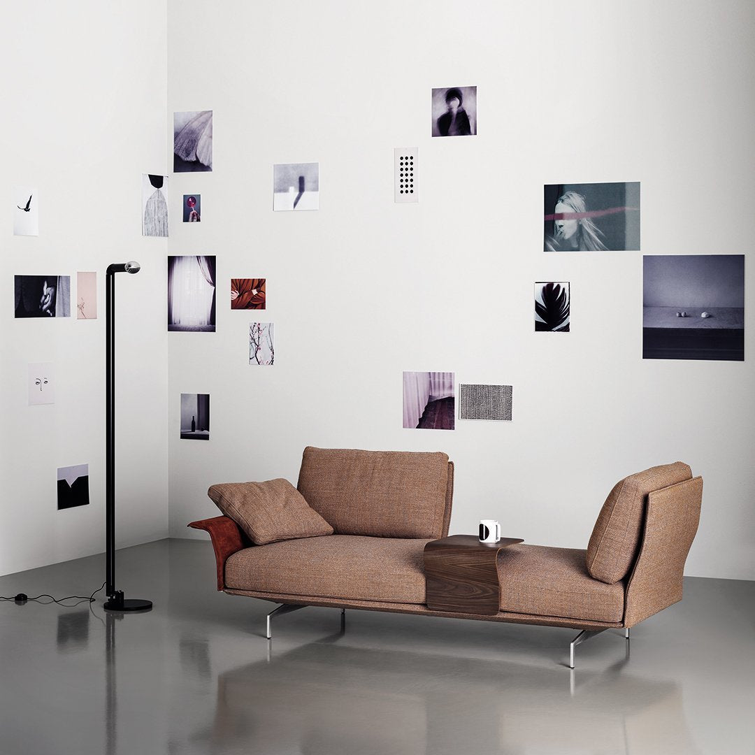 Modern brown fabric sofa with sleek lines, paired with a minimalist black floor lamp against a gallery wall of grayscale photos.