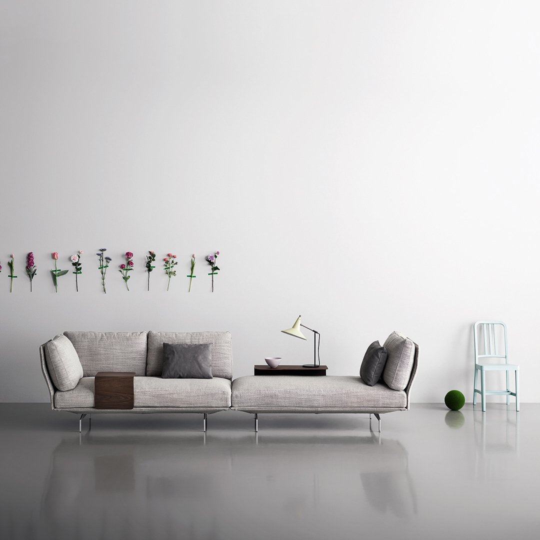 Grey textured sofa with soft pillows, minimalist design, against a white wall with floral accents and a light blue chair.