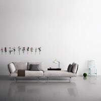 Grey textured sofa with soft pillows, minimalist design, against a white wall with floral accents and a light blue chair.