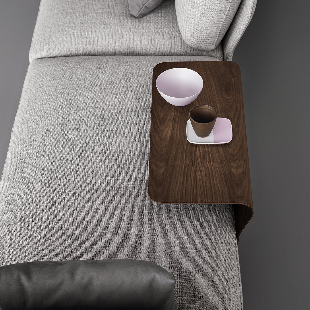 Brown wooden side table on a gray textured couch with a pink bowl and cup, showcasing minimalist design.