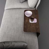 Dark wood side table with smooth finish, paired with soft gray fabric and pastel-colored bowls and cups.