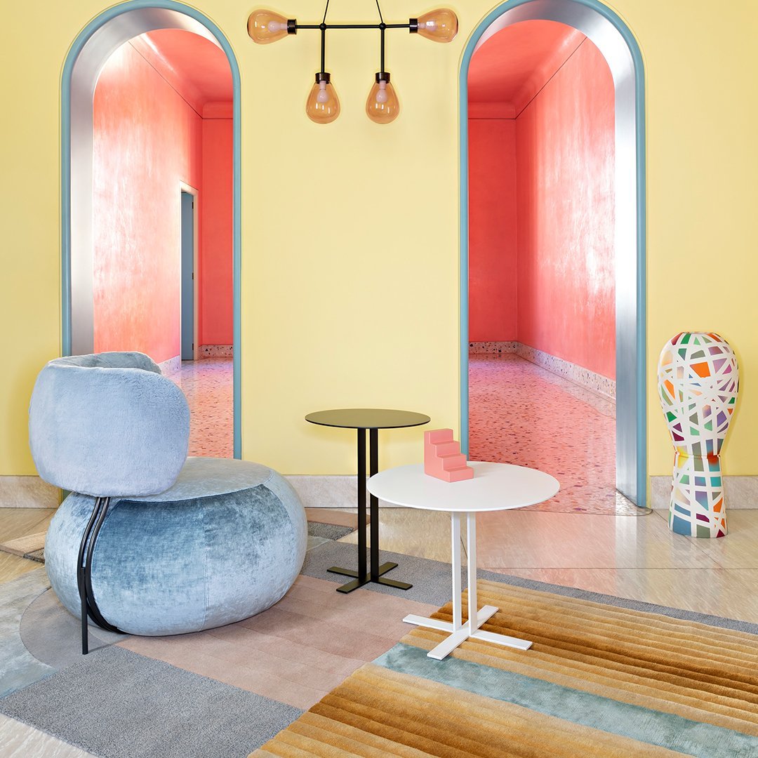 Vibrant yellow walls, pink arches, blue velvet chair, white modern table, and colorful patterned decor enhance this stylish room.