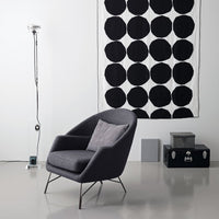 Gray armchair in front of a black and white patterned wall hanging with large circles. Modern minimalist decor.