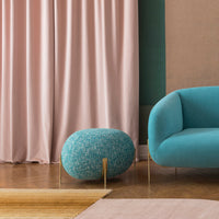 "Turquoise sofa and pouf with textured aqua pattern, against soft pink curtains and warm wood flooring."