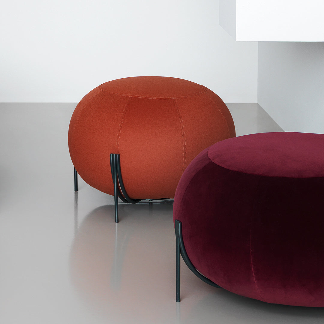 "Elegant round ottomans in bold rust and deep burgundy upholstery, featuring sleek black legs."