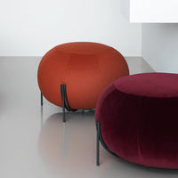 "Elegant round ottomans in bold rust and deep burgundy upholstery, featuring sleek black legs."