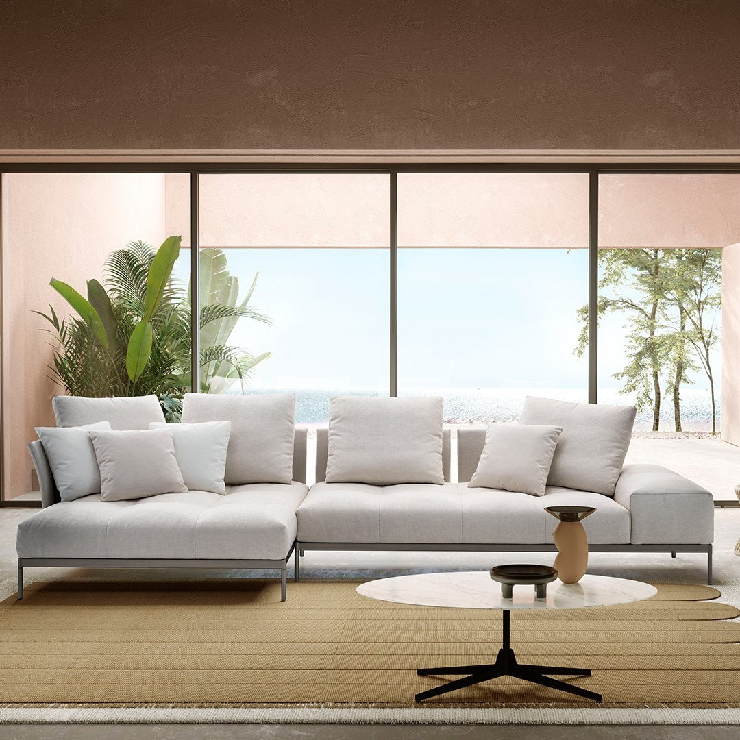 Modern white sectional sofa with plush cushions, set against a neutral backdrop and natural greenery. Clean lines, minimalist design.