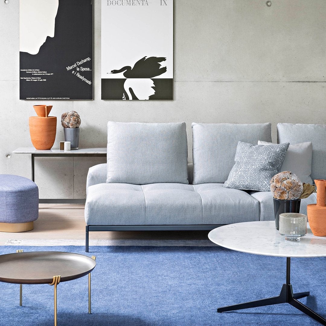Light blue sofa with grey cushions on a vibrant blue rug, accented by terracotta vases and a white round table.