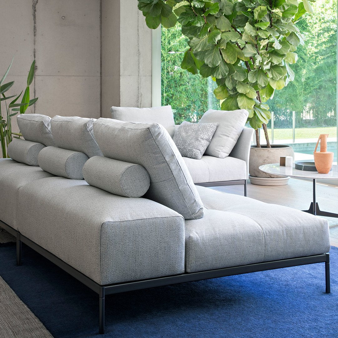 Contemporary gray sofa with textured upholstery and cylindrical cushions, set against a blue area rug.