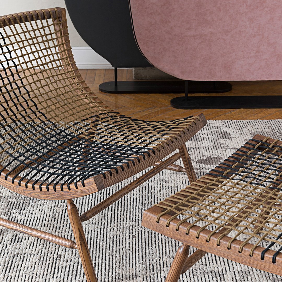 Natural wood frame lounge chair with black and tan woven patterns, paired with a minimalist rug in neutral tones.