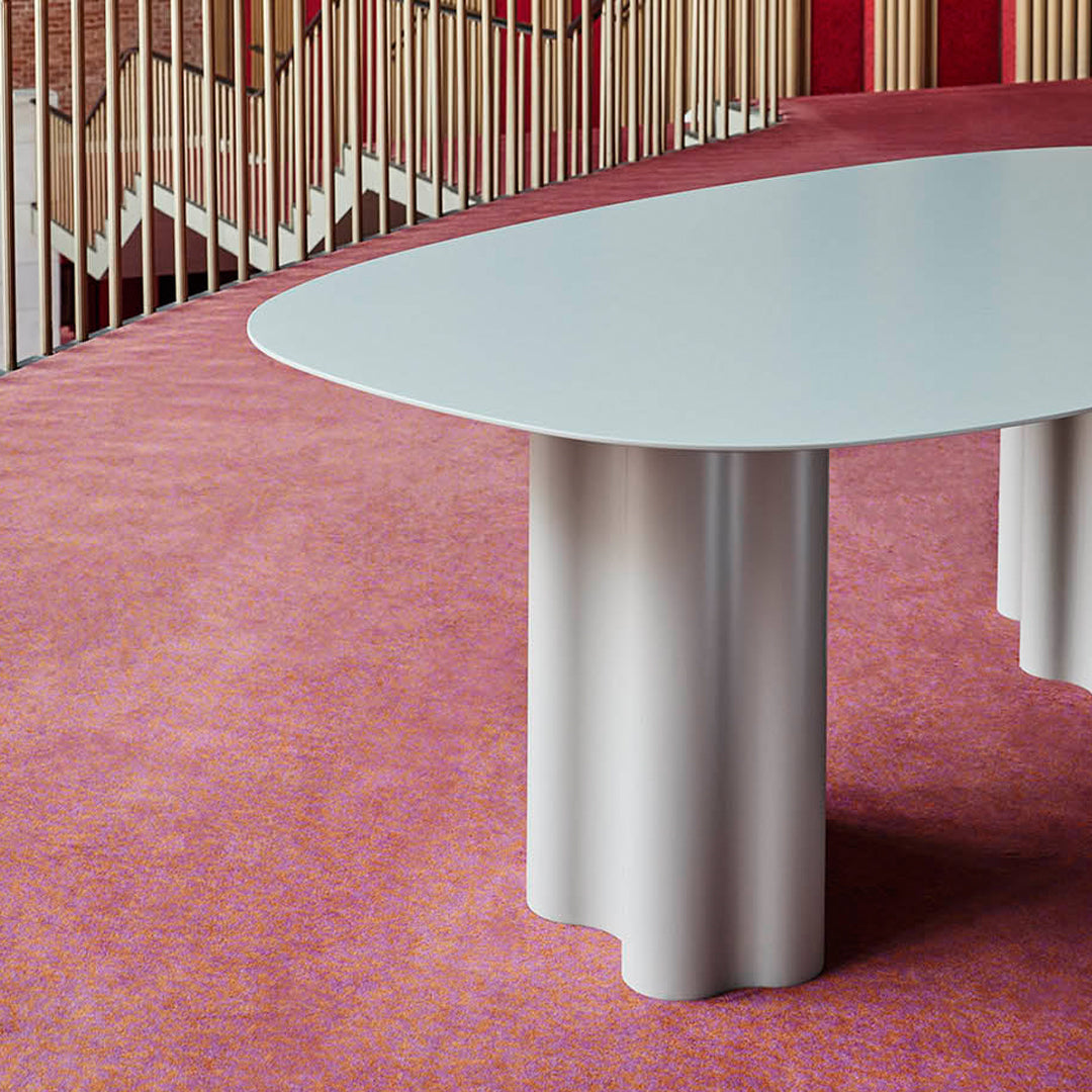"Light blue oval table on a textured pink carpet, featuring subtle purple and orange patterns."