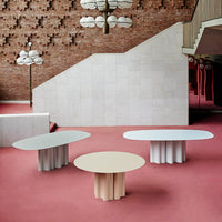 Three contemporary coffee tables in pastel blue, soft beige, and light grey on a pink carpeted floor.