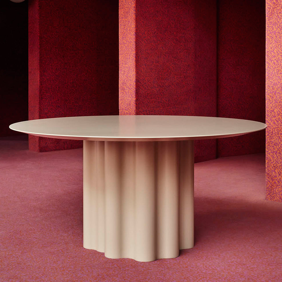 Beige round table with a fluted base, set against a textured red background. Modern design with soft curves.