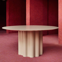 Beige round table with a fluted base, set against a textured red background. Modern design with soft curves.