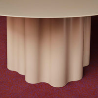 Beige scalloped table base on a red patterned rug. Elegant, modern design with smooth textures.