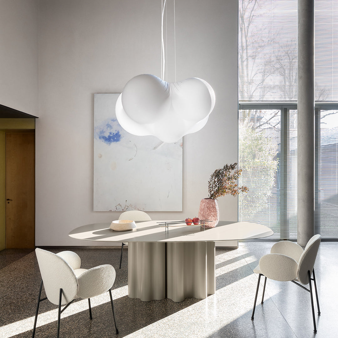 Modern white pendant light above a curved beige dining table, complemented by soft white chairs and a pastel wall art.