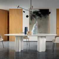 Modern white round dining table with smooth surfaces against a minimalist interior featuring earthy wood tones.
