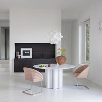 Modern dining area featuring a round white table, soft pink chairs, and a textured brown vase against a neutral backdrop.