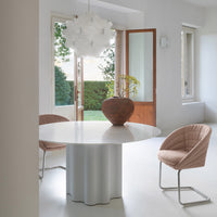 Modern round white table with a textured gray base, paired with soft pink chairs in a bright, minimalist room.