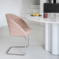 Pink upholstered chair with curved design against a modern white table and light floor. Simple and elegant aesthetic.