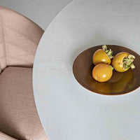 Round light blue table with a bronze plate and three yellow persimmons, complemented by a light pink chair.