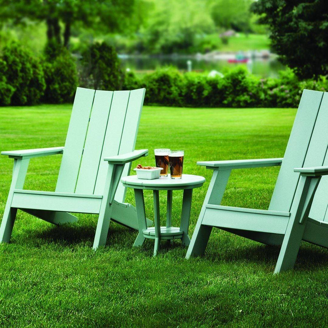 Light green Adirondack chairs paired with a matching side table on a lush green lawn, perfect for outdoor relaxation.