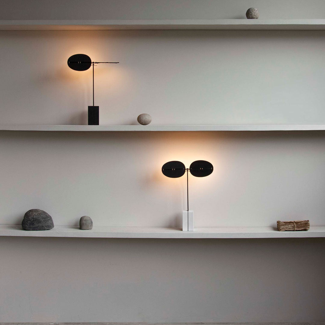 Modern black and white lamps on minimalist shelves, featuring warm glow and earthy stone accents.