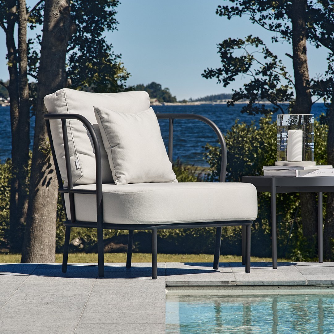 Light grey upholstered chair with black metal frame, set against a scenic outdoor backdrop by the pool.