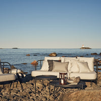 Coastal patio furniture in soft beige and gray tones, featuring minimalist patterns against a serene ocean backdrop.