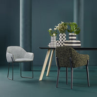 Stylish gray and green chairs with geometric patterned vases on a modern table, set against a dark teal background.
